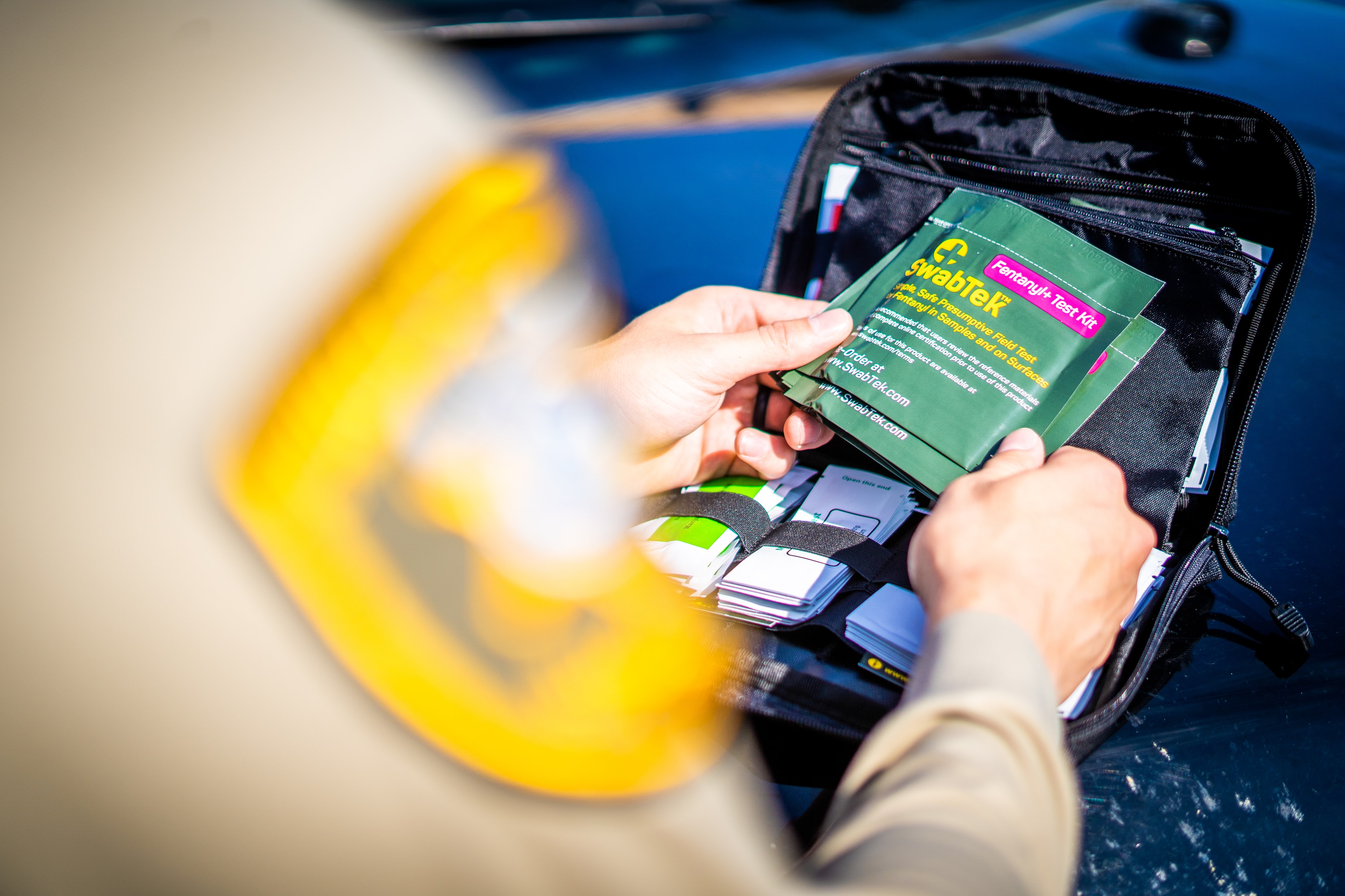 An officer selects a SwabTek Fentanyl+ kit from a field bag