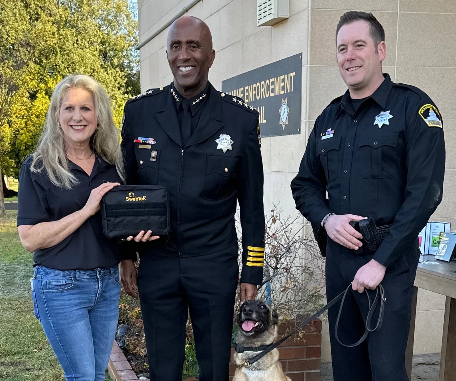 SwabTek representative with Sacramento sheriff’s personnel and a police dog at a kit presentation.